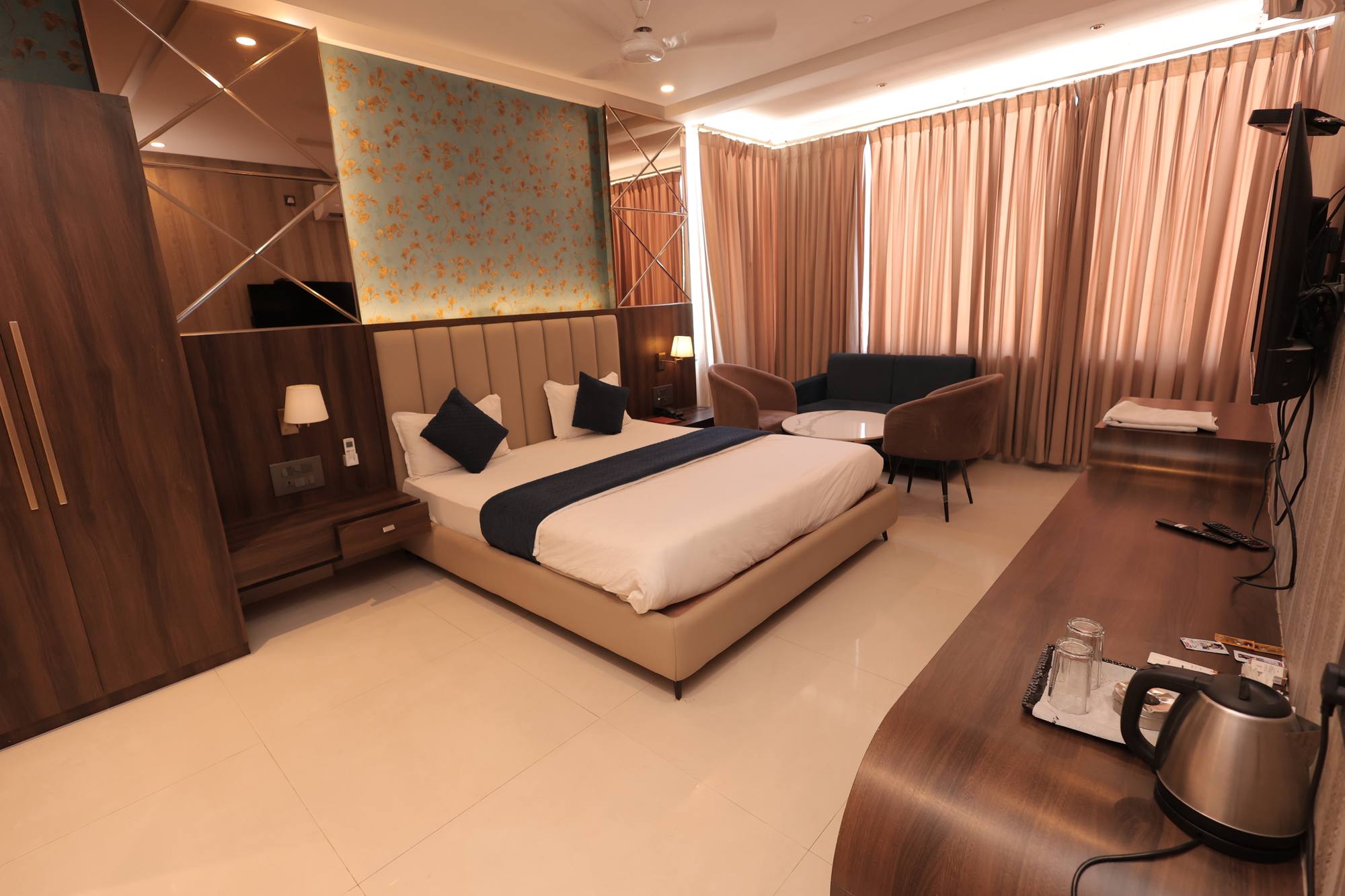 The Premium Room at Hotel Relax Inn, Banswara — king bed against a gold floral feature wall, with a seating area and work desk